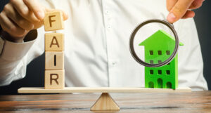 picture illustrating fair housing with letter blocks balanced against a house under a magnifying glass